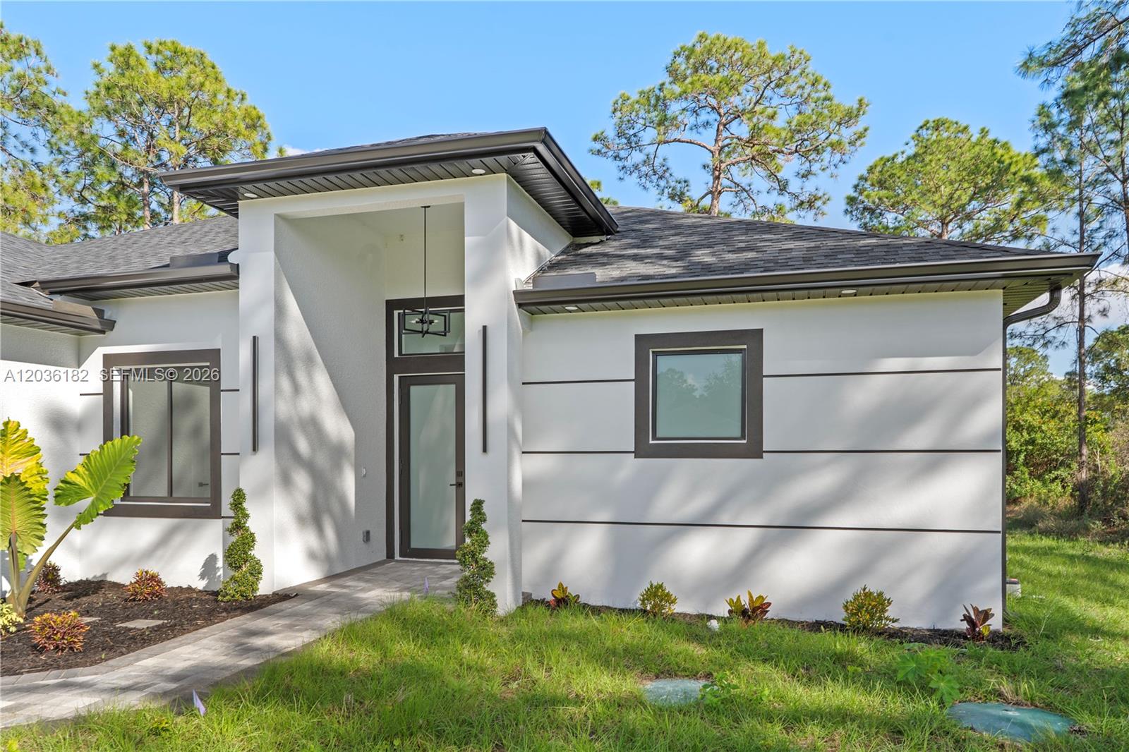 A modern single-story house exterior features white stucco walls with horizontal trim and a covered entryway — 1116 EIGHTH AVE, Lehigh Acres FL 33972, LEHIGH ACRES, FL