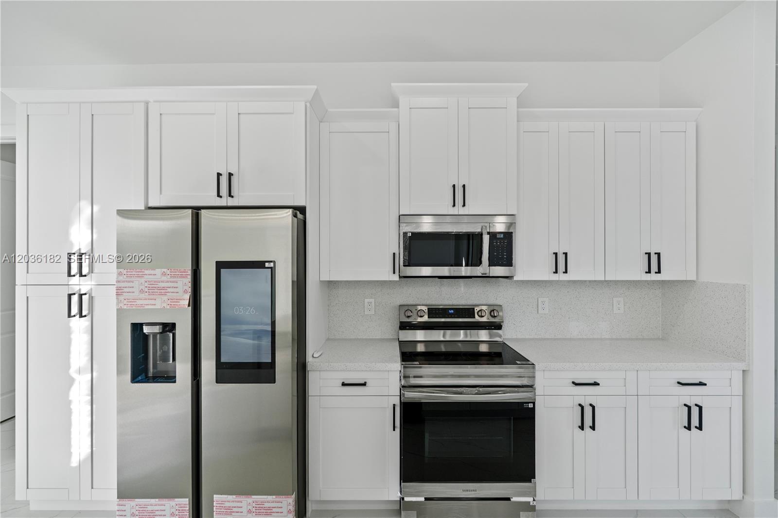 A modern kitchen features white shaker cabinets, stainless steel appliances, and light-colored quartz countertops — 1116 EIGHTH AVE, Lehigh Acres FL 33972, LEHIGH ACRES, FL