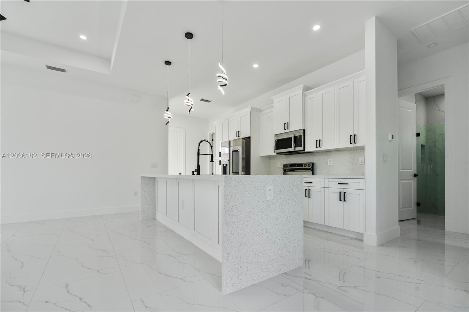 A modern kitchen features white cabinetry, a speckled quartz island, and marble-look tile flooring — 1116 EIGHTH AVE, Lehigh Acres FL 33972, LEHIGH ACRES, FL