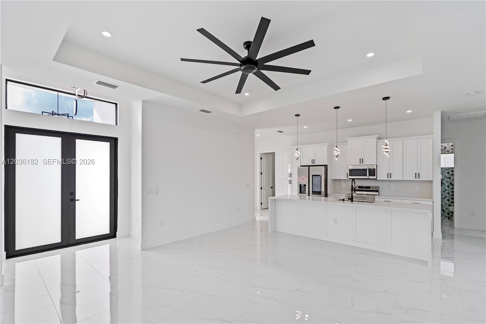 A modern, open-concept kitchen and living area features white cabinetry, marble-look tile floors, and a ceiling fan — 1116 EIGHTH AVE, Lehigh Acres FL 33972, LEHIGH ACRES, FL