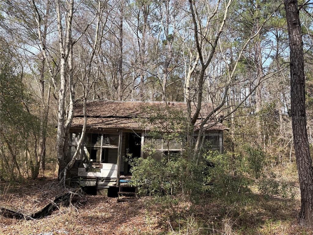 A dilapidated wooden cabin with a screened porch sits among trees in a wooded area — 4385 BONDARENKO ROAD, KEYSTONE HEIGHTS, FL