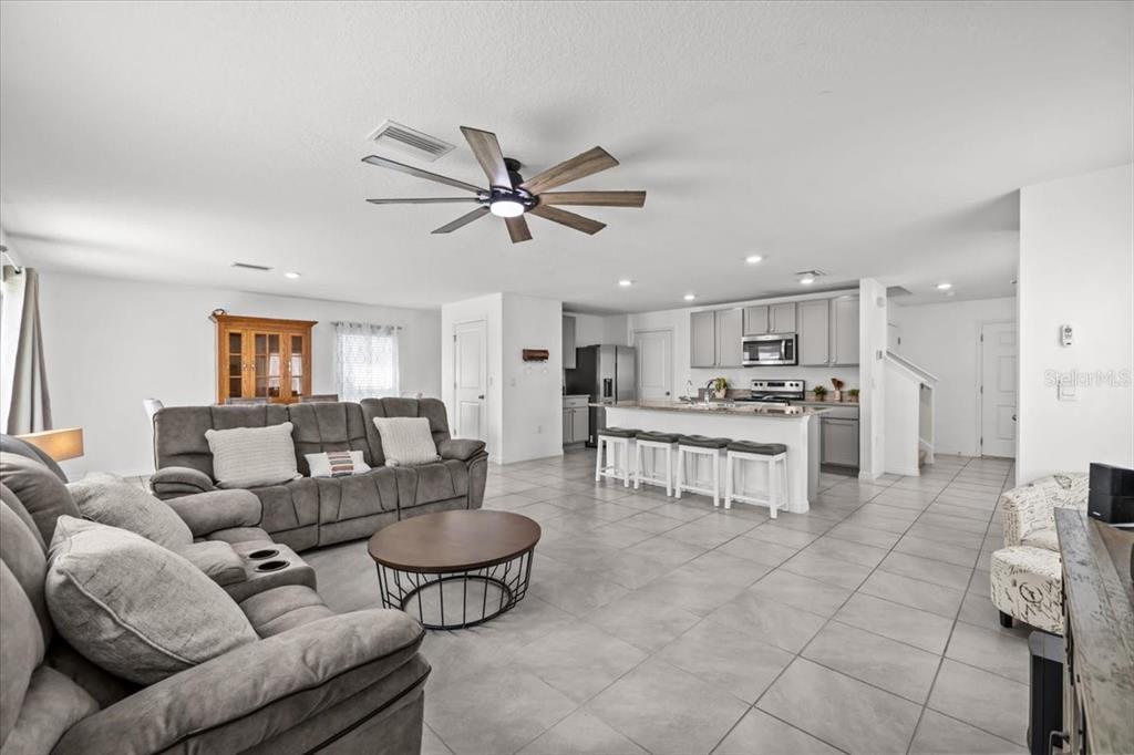 An open-concept living room and kitchen featuring grey tile flooring and a ceiling fan — 12148 WHITE CYPRESS PLACE, RIVERVIEW, FL