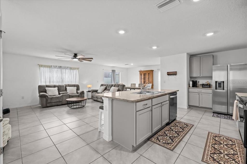 An open-concept kitchen and living room with gray cabinets, granite countertops, and tile flooring — 12148 WHITE CYPRESS PLACE, RIVERVIEW, FL