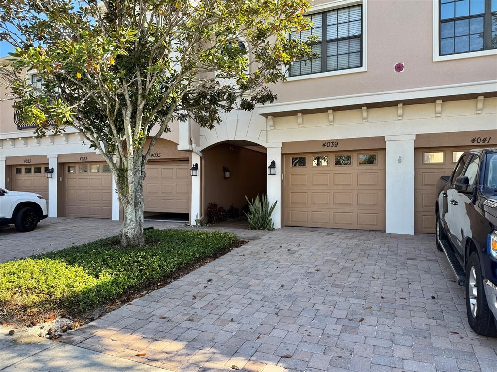 The exterior view shows a row of townhomes with tan garages and a paved driveway — 4037 OVERTURE CIRCLE UNIT 4037, BRADENTON, FL