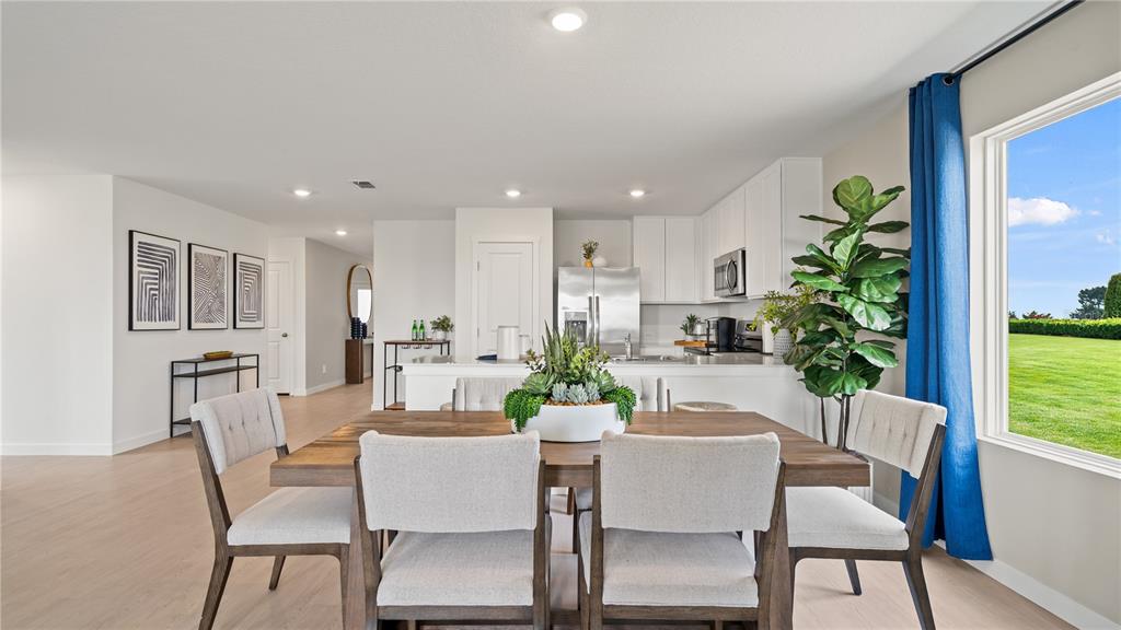 A dining area with a wooden table and chairs sits before an open-concept white kitchen — 315 NOLA LANE, DUNDEE, FL