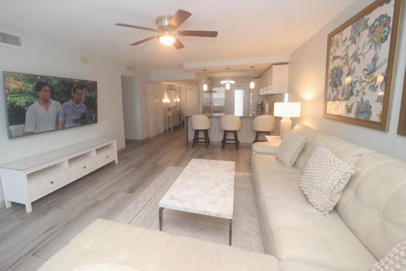A living room with a white sectional sofa, marble coffee table, and wall-mounted television — 3091 N Course Drive # 303, Pompano Beach FL 33069, POMPANO BEACH, FL