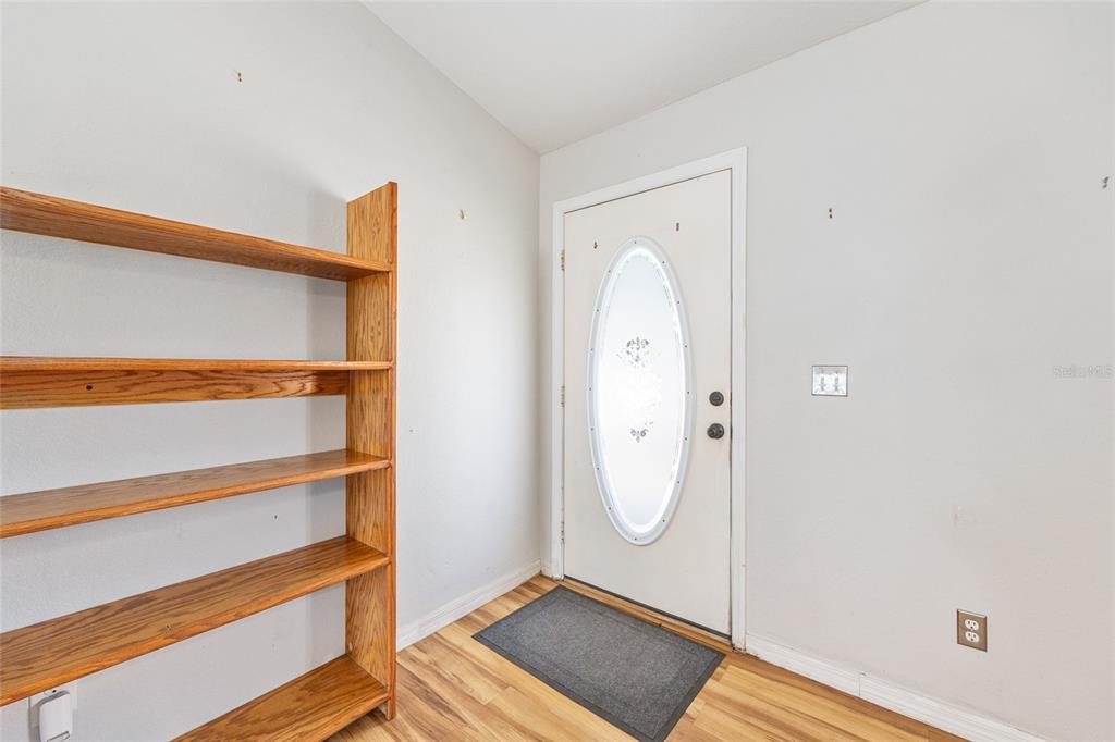 An entryway features light gray walls, wood-look flooring, a wooden bookshelf, and a white front door — 10 PECAN RADIAL TRACE, OCALA, FL