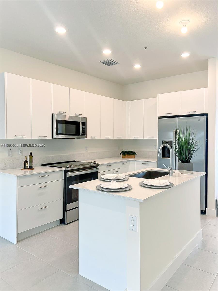 A modern kitchen features white cabinetry, stainless steel appliances, and a central island with seating — 8001 NW 41st St # 206, Doral FL 33166, DORAL, FL