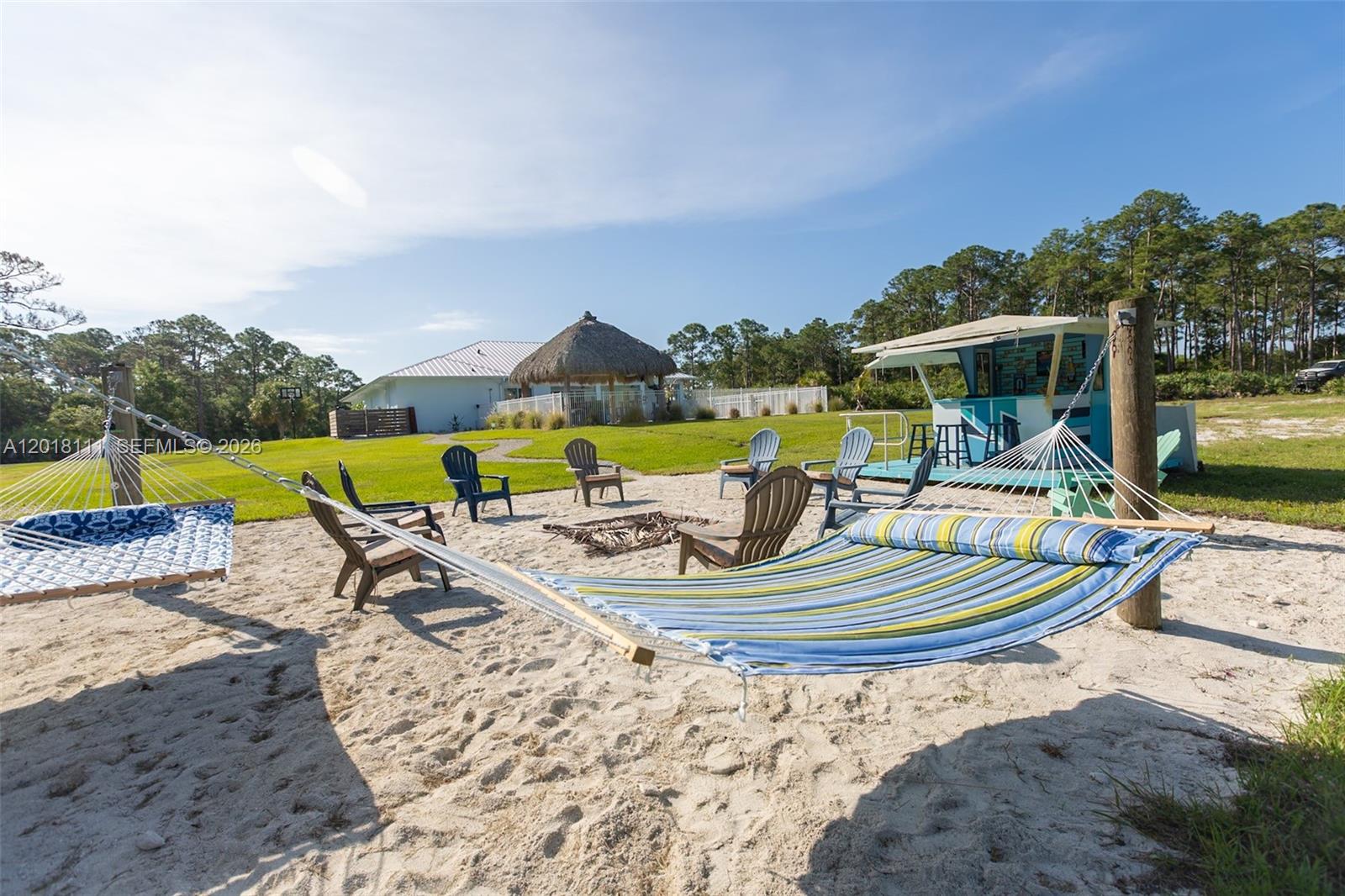 A sandy backyard area features hammocks, Adirondack chairs, a fire pit, and a tiki bar — 5371 S 25th St, Fort Pierce FL 34981, FORT PIERCE, FL