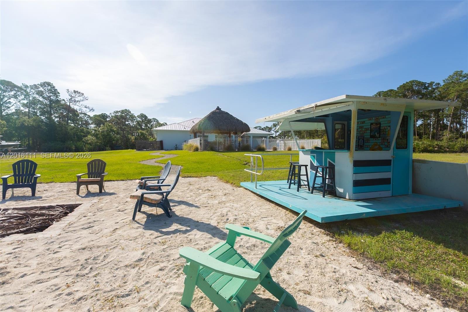 A sandy backyard features a tiki bar, several Adirondack chairs, and a fire pit area — 5371 S 25th St, Fort Pierce FL 34981, FORT PIERCE, FL