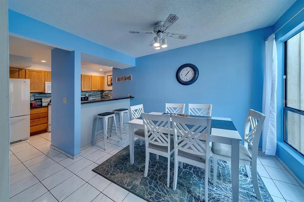 A dining area with a white table and chairs sits next to a kitchen with bar seating — 6157 MIDNIGHT PASS ROAD UNIT D32, SARASOTA, FL