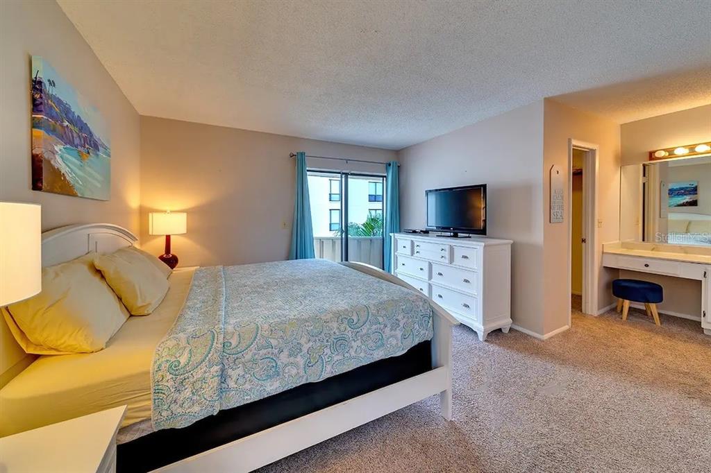 A bedroom with a king bed, white dresser, television, and a vanity area with a mirror — 6157 MIDNIGHT PASS ROAD UNIT D32, SARASOTA, FL