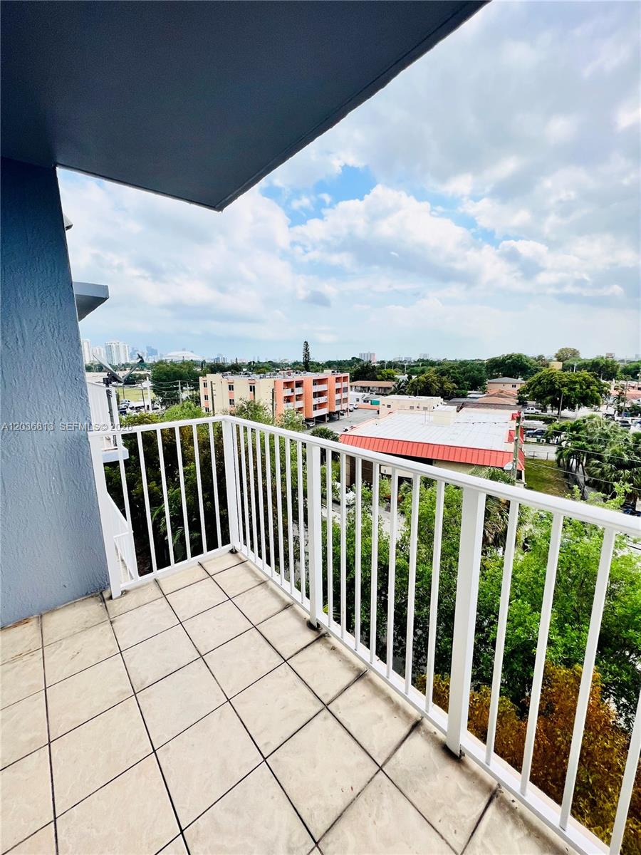 A tiled balcony with a white railing overlooks a suburban area with buildings and trees — 2415 NW 16th St Rd # 1, Miami FL 33125, MIAMI, FL