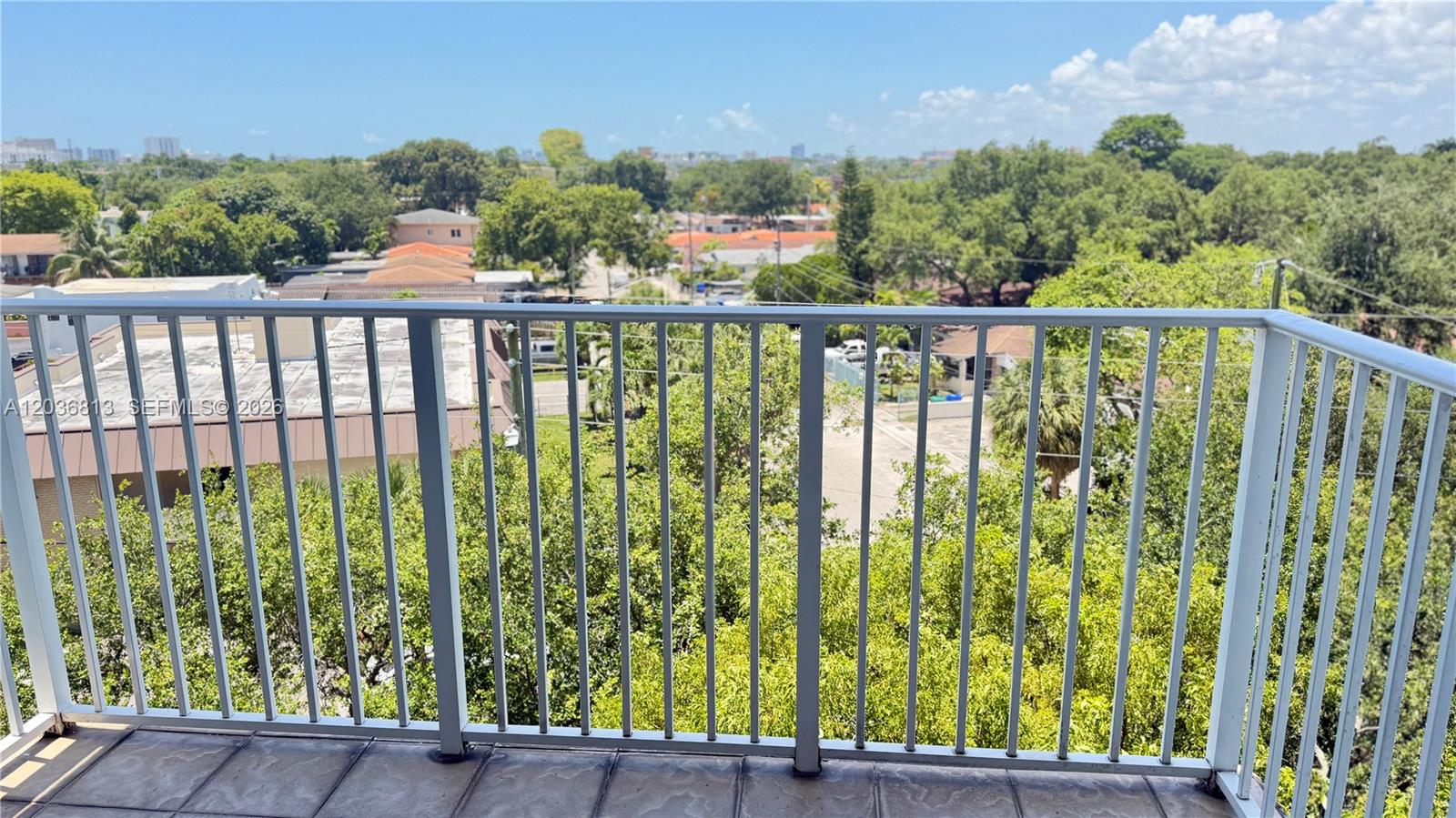 A balcony with a white metal railing overlooks a neighborhood with trees and buildings — 2415 NW 16th St Rd # 1, Miami FL 33125, MIAMI, FL