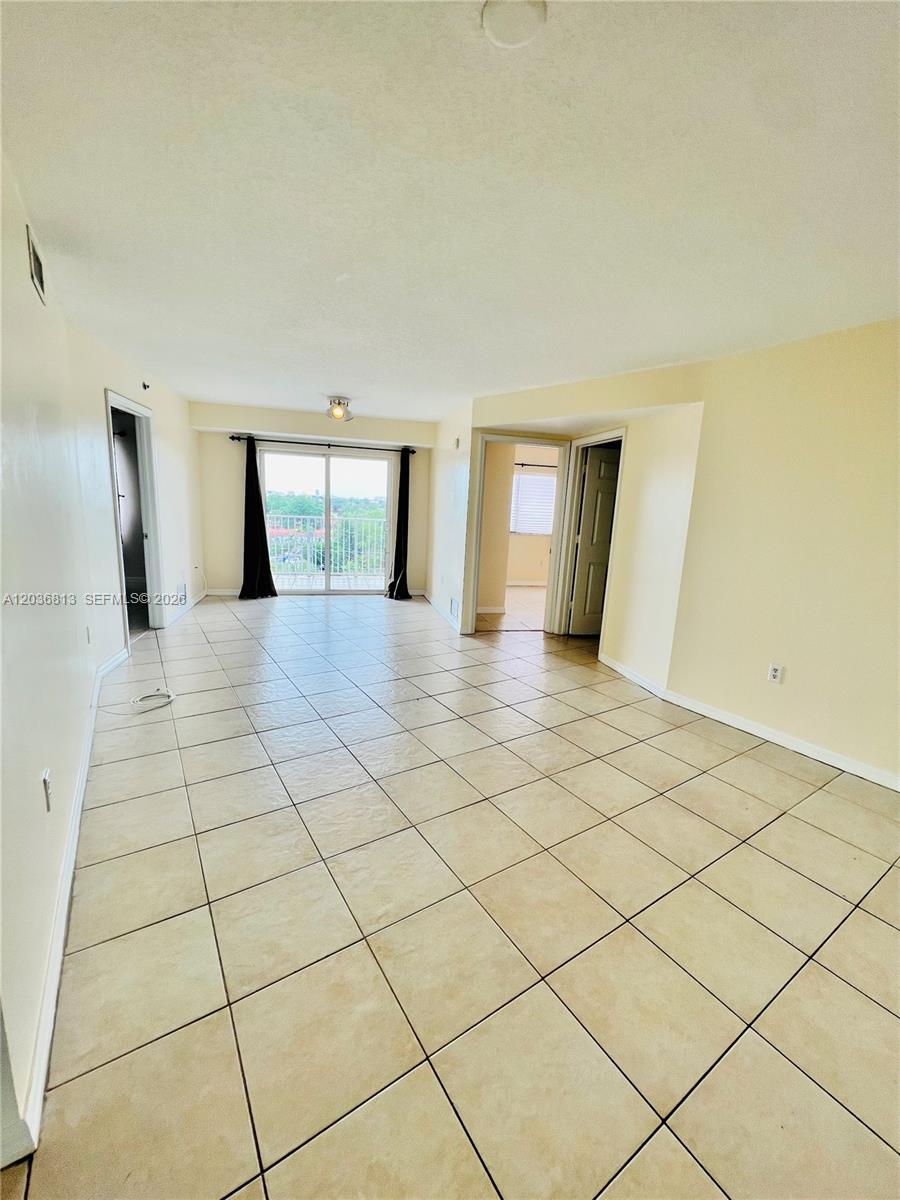 A bright, empty living room features beige tile flooring, white walls, and a sliding glass door — 2415 NW 16th St Rd # 1, Miami FL 33125, MIAMI, FL