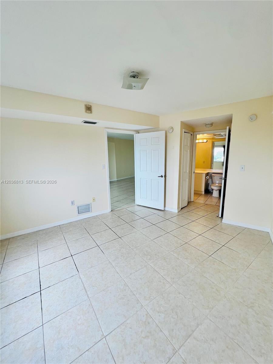 A room with light-colored tile flooring, a white door, and an open bathroom doorway — 2415 NW 16th St Rd # 1, Miami FL 33125, MIAMI, FL