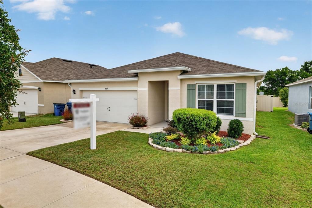 A single-story suburban house with a tan stucco exterior, a two-car garage, and landscaping — 524 BOARDWALK AVENUE, HAINES CITY, FL