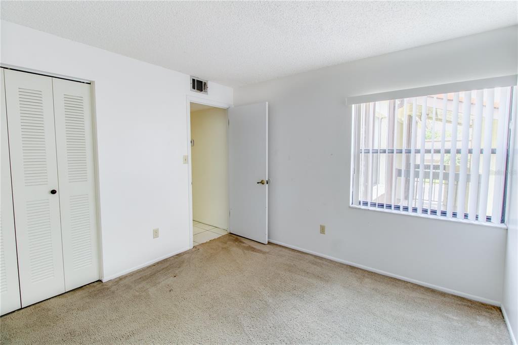 An empty bedroom features beige carpet, white walls, a closet, and a window with blinds — 3293 WESTRIDGE BOULEVARD UNIT 203, ORLANDO, FL