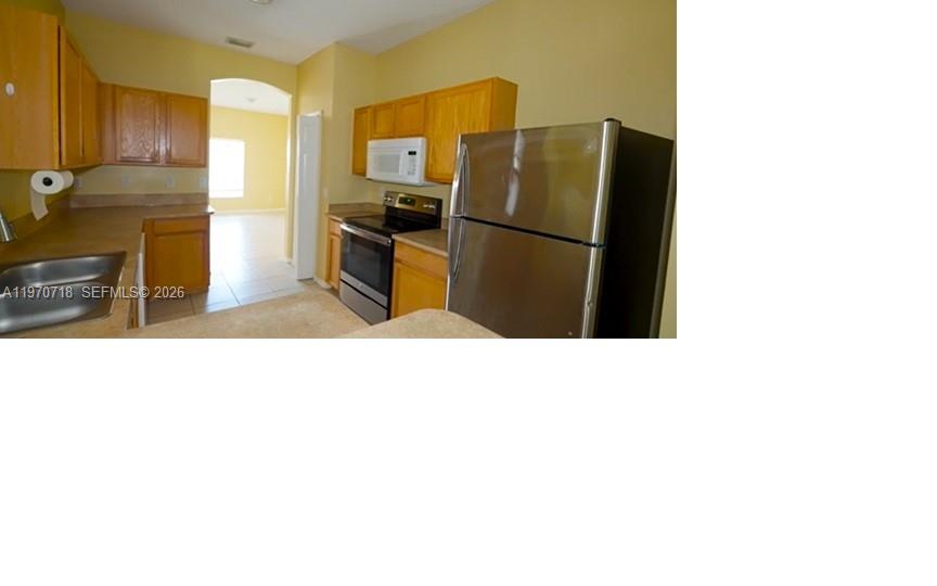 This kitchen features light wood cabinets, stainless steel appliances, and tan countertops — 8720 97th Ave, Vero Beach FL 32967, VERO BEACH, FL