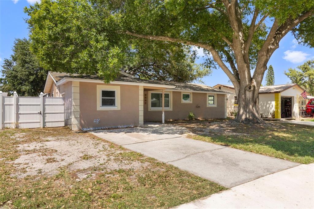 A single-story tan house with a concrete driveway and a large tree in the yard — 5557 146TH TERRACE N, CLEARWATER, FL