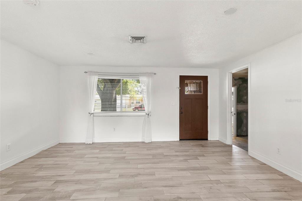 A living room with white walls, light wood-look tile flooring, a window, and a brown door — 5557 146TH TERRACE N, CLEARWATER, FL