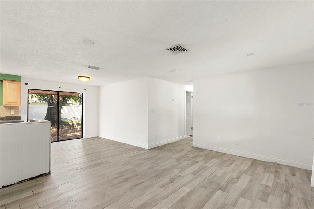 An open-concept living area features light wood-look tile flooring, white walls, and a sliding door — 5557 146TH TERRACE N, CLEARWATER, FL