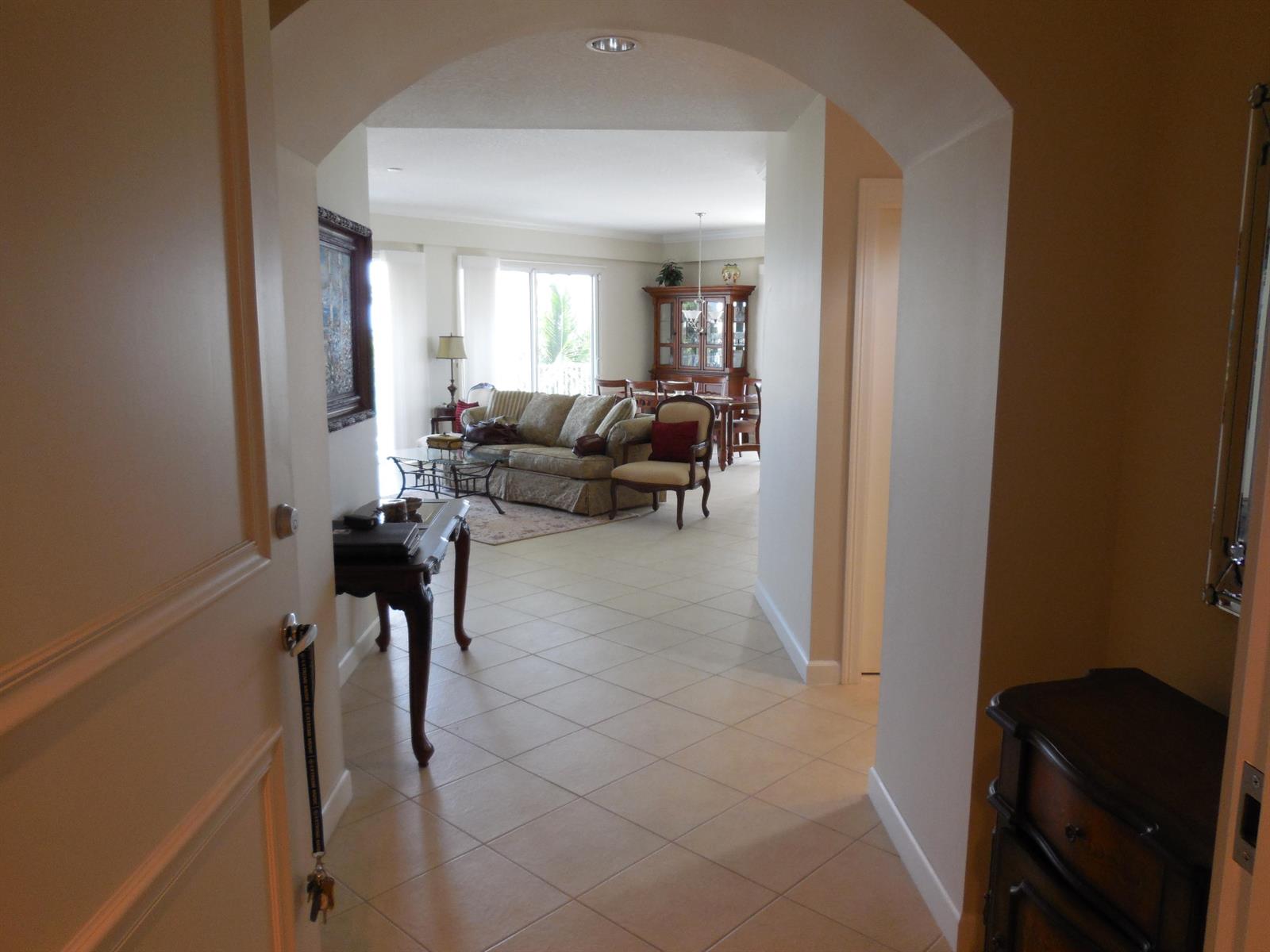 A view through an arched entryway into a tiled living room with traditional furniture — 800 Juno Ocean Walk # 301a, Juno Beach FL 33408, JUNO BEACH, FL