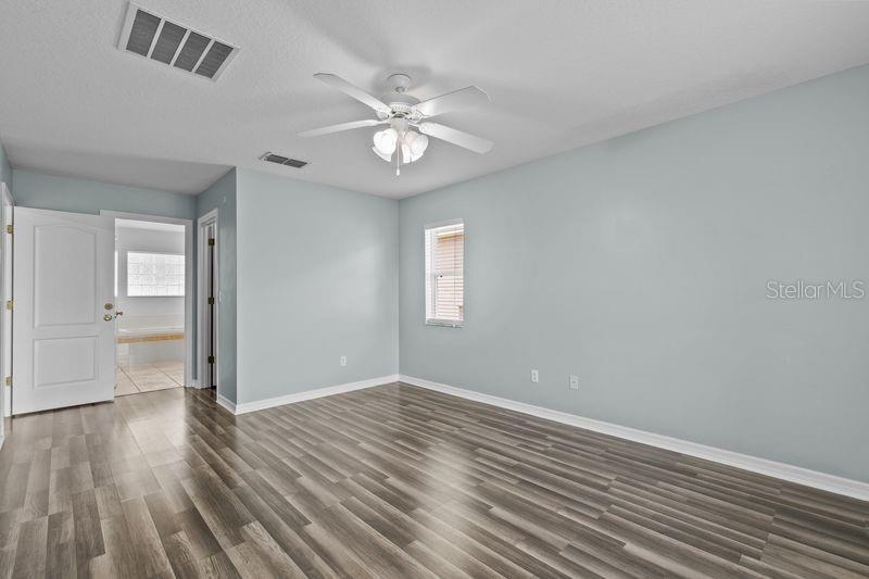 An empty bedroom features light blue walls, wood-look flooring, a ceiling fan, and a doorway — 214 COMPASS ROSE DRIVE, GROVELAND, FL