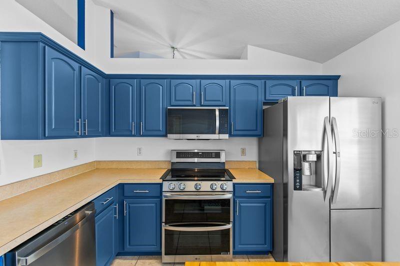 A kitchen features blue cabinets, stainless steel appliances, and tan countertops — 214 COMPASS ROSE DRIVE, GROVELAND, FL