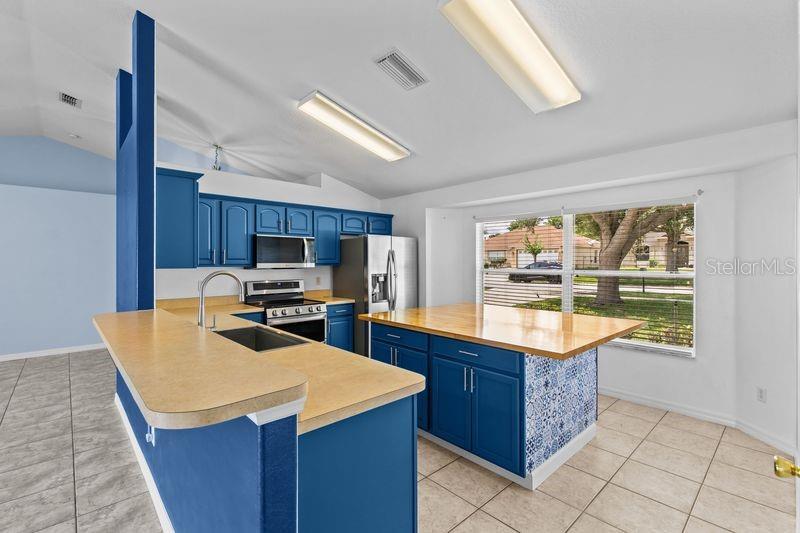 A kitchen features blue cabinets, a wooden island countertop, and a beige laminate peninsula — 214 COMPASS ROSE DRIVE, GROVELAND, FL