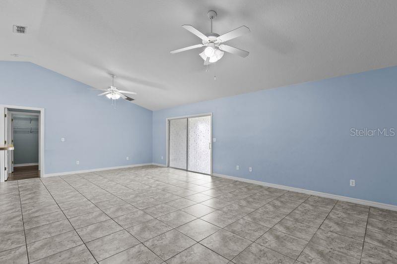 A spacious room with light blue walls, tiled floors, two ceiling fans, and sliding glass doors — 214 COMPASS ROSE DRIVE, GROVELAND, FL