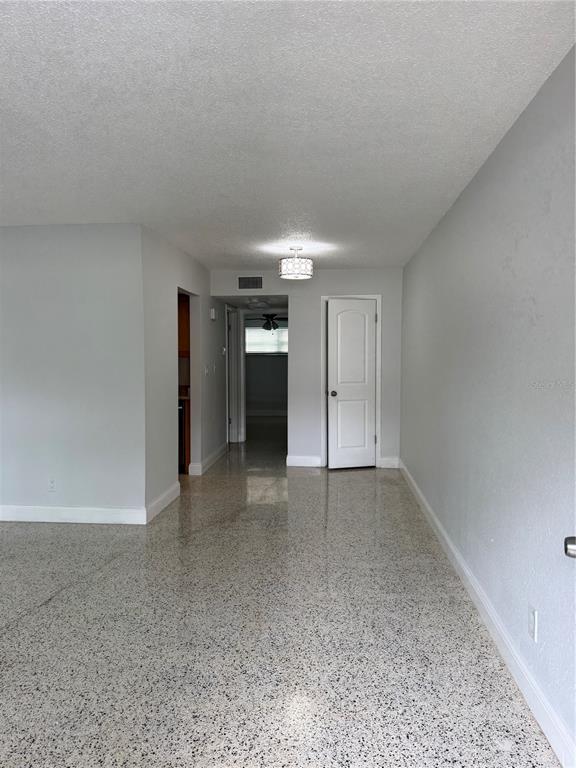 A room with light gray walls, white trim, and speckled terrazzo flooring leads to a hallway — 4200 1ST STREET UNIT 2, ST PETERSBURG, FL
