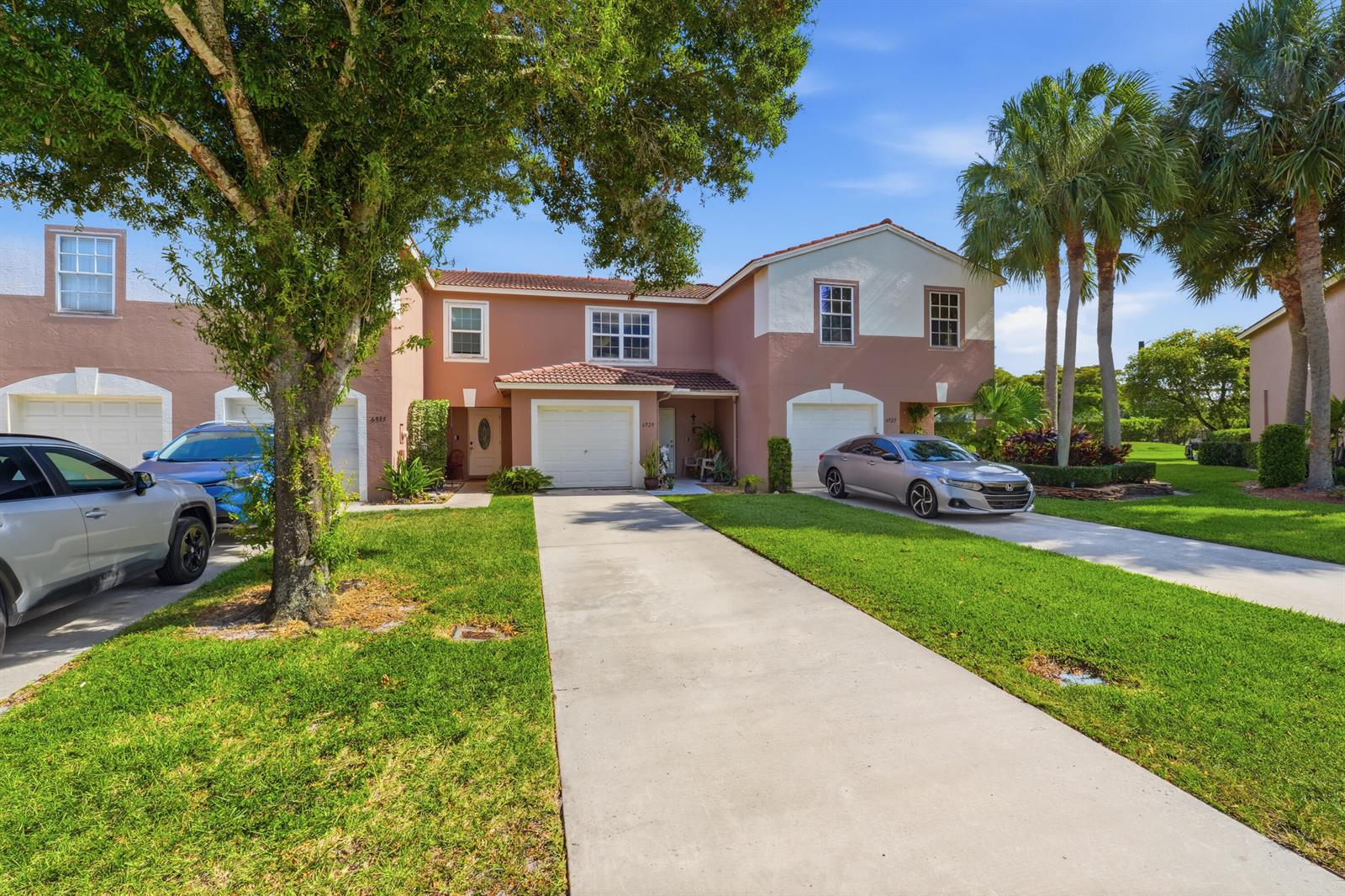 A two-story townhouse with a peach-colored exterior, two garage doors, and a concrete driveway — 6929 Willow Creek Run, Lake Worth FL 33463, LAKE WORTH, FL