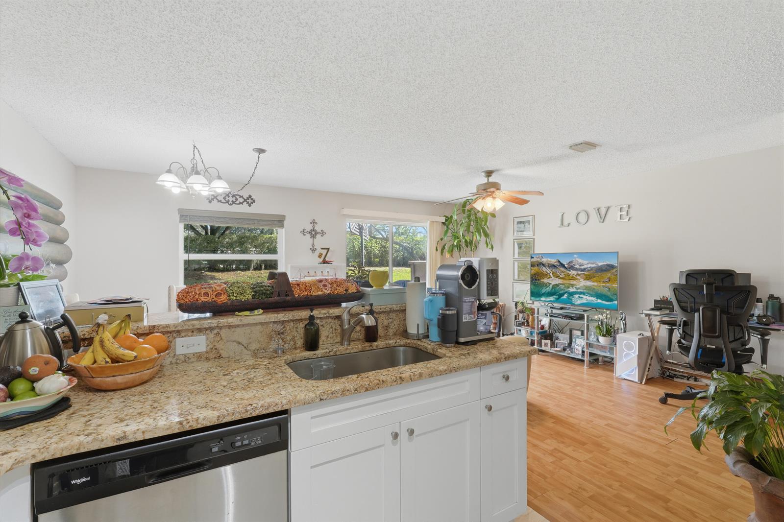 A kitchen with granite countertops and white cabinets overlooks a living area with wood flooring — 6929 Willow Creek Run, Lake Worth FL 33463, LAKE WORTH, FL