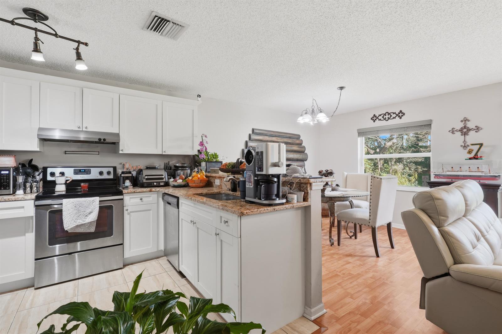 A kitchen with white cabinets and granite countertops opens to a dining area and living space — 6929 Willow Creek Run, Lake Worth FL 33463, LAKE WORTH, FL