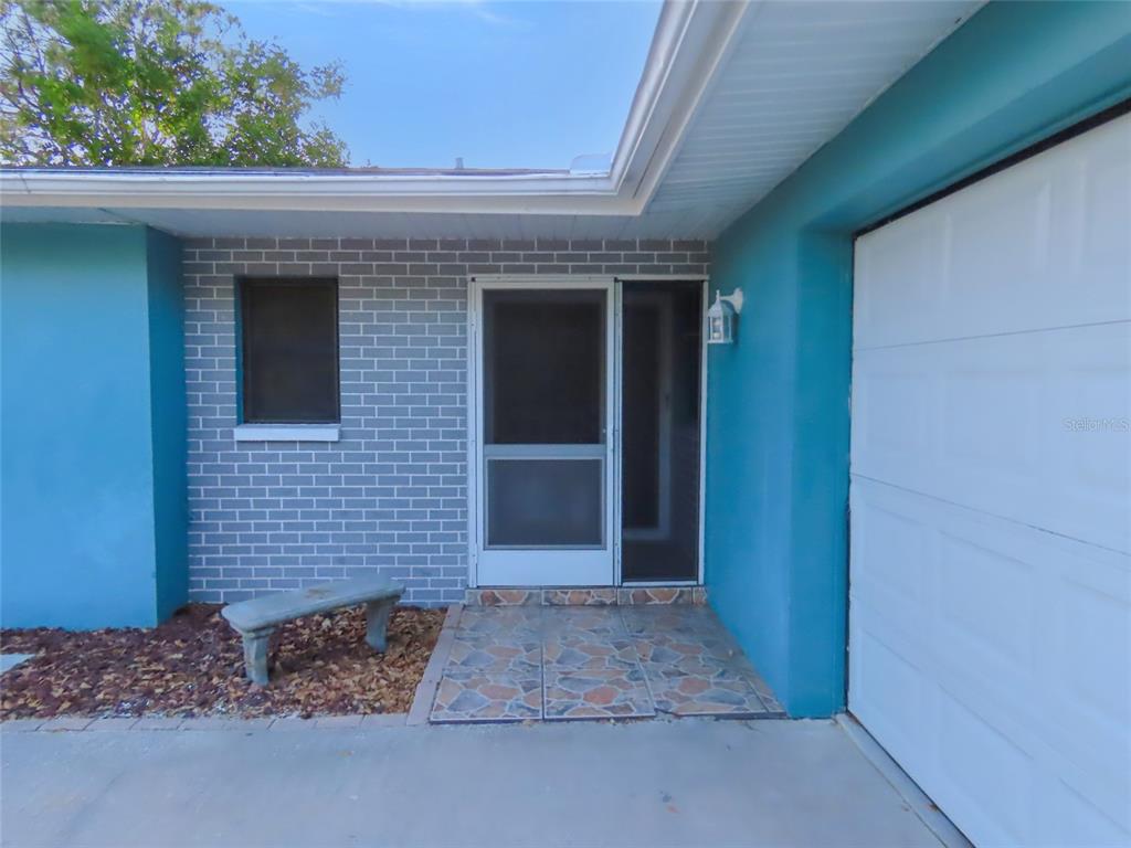 The exterior of a house features a blue wall, gray brick, a screen door, and bench — 1798 FAULDS ROAD N, CLEARWATER, FL