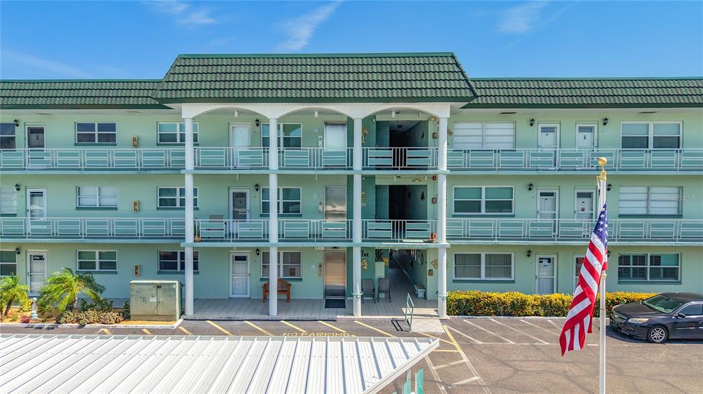 A three-story, light green apartment building features white railings and a green tiled roof — 5935 30TH AVENUE S UNIT 104, GULFPORT, FL