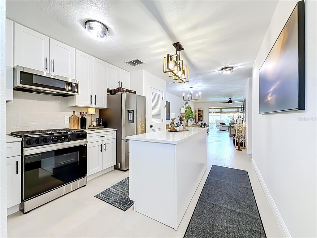 A modern kitchen features white cabinetry, stainless steel appliances, a central island, and tile flooring — 5935 30TH AVENUE S UNIT 104, GULFPORT, FL