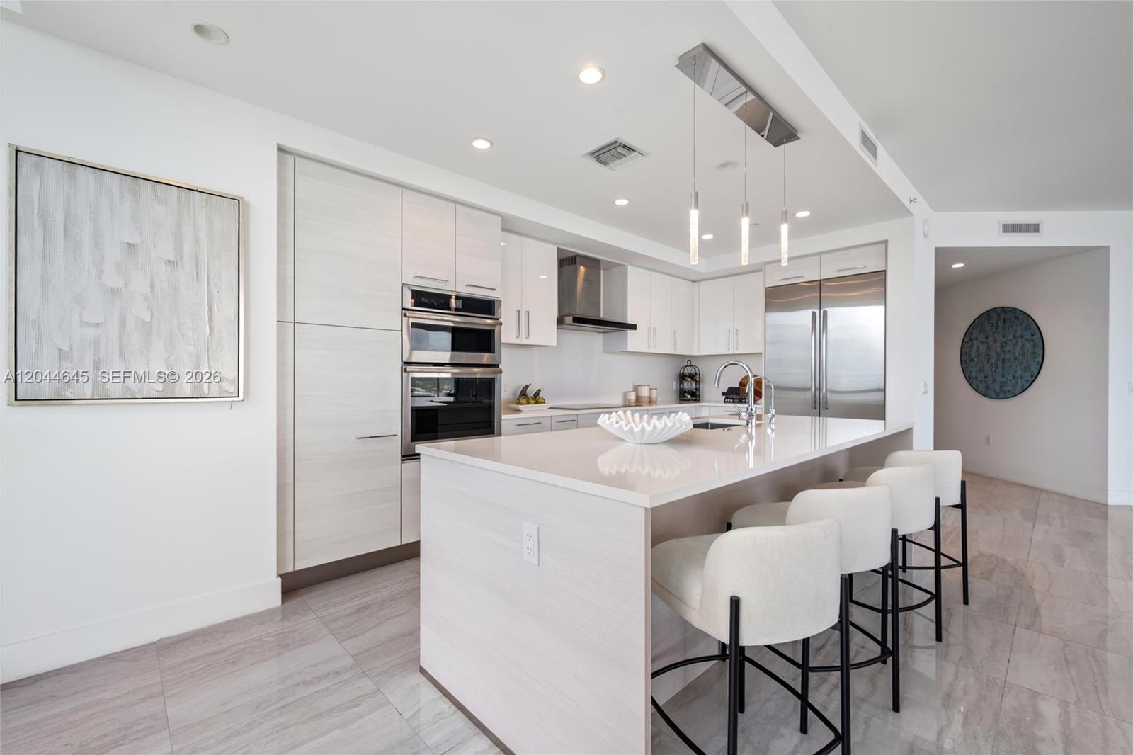 A modern kitchen features light wood cabinetry, white countertops, a central island, and bar stools — 100 E Las Olas Blvd # 3201, Fort Lauderdale FL 33301, FORT LAUDERDALE, FL