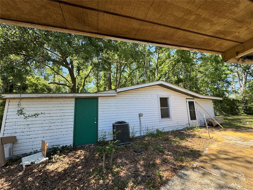 The exterior of a white, single-story house features a green door and an air conditioning unit — 15130 N 104TH STREET, LIVE OAK, FL