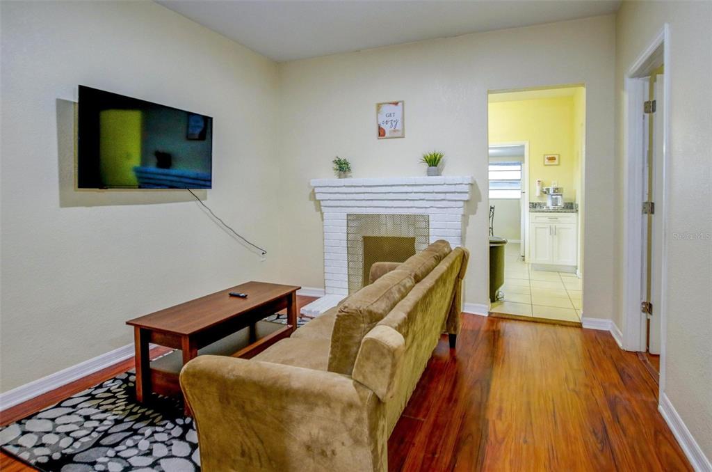 A living room features a white brick fireplace, a brown sofa, and wood flooring — 1219 E EMMA STREET, TAMPA, FL