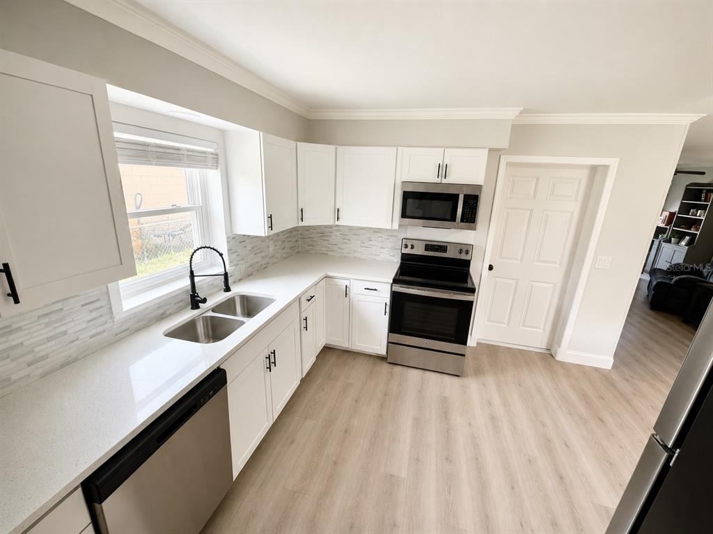 A kitchen with white cabinets, stainless steel appliances, quartz countertops, and light wood-look flooring — 300 S BUENA VISTA AVENUE, ORLANDO, FL