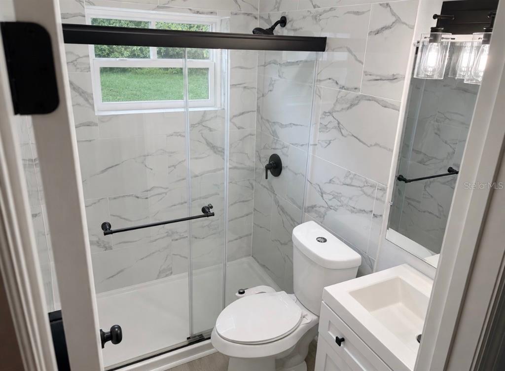 A small bathroom features a glass-enclosed shower, marble-look tile walls, and a white vanity — 300 S BUENA VISTA AVENUE, ORLANDO, FL