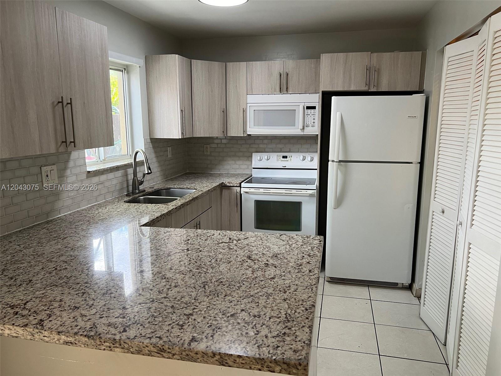 A kitchen features light wood cabinets, granite countertops, white appliances, and a tiled backsplash — 6975 NW 173rd Dr # 2007, Hialeah FL 33015, HIALEAH, FL