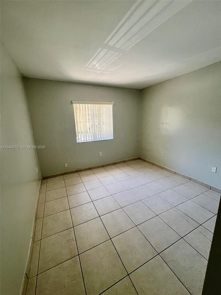 An empty bedroom features light-colored walls, a single window with blinds, and tiled flooring — 6975 NW 173rd Dr # 2007, Hialeah FL 33015, HIALEAH, FL