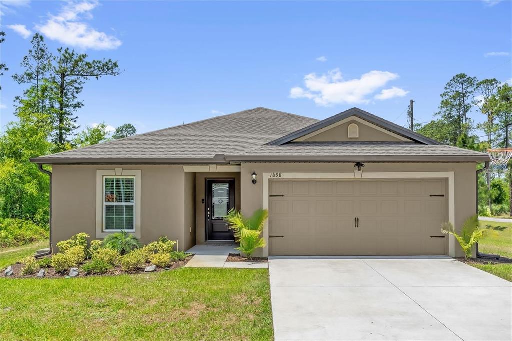 A single-story house with a tan stucco exterior, a two-car garage, and a front lawn — 1898 9TH AVENUE, DELAND, FL