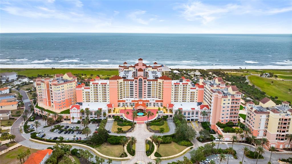 An aerial view of a large, multi-story peach-colored resort hotel situated on a sandy beach — 200 OCEAN CREST DRIVE UNIT 217, PALM COAST, FL