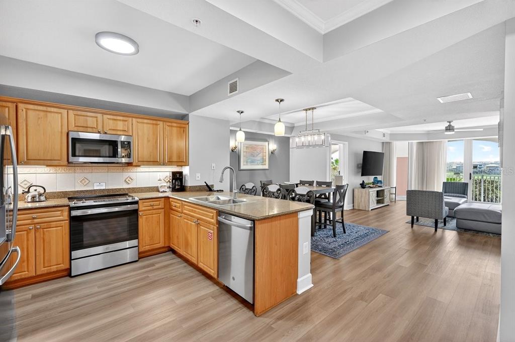 A kitchen with wooden cabinets and granite countertops opens into a dining and living area — 200 OCEAN CREST DRIVE UNIT 217, PALM COAST, FL