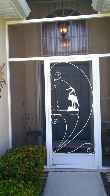 A white metal screen door with a heron design leads to a dark blue front door — 1640 PALACE COURT, PUNTA GORDA, FL