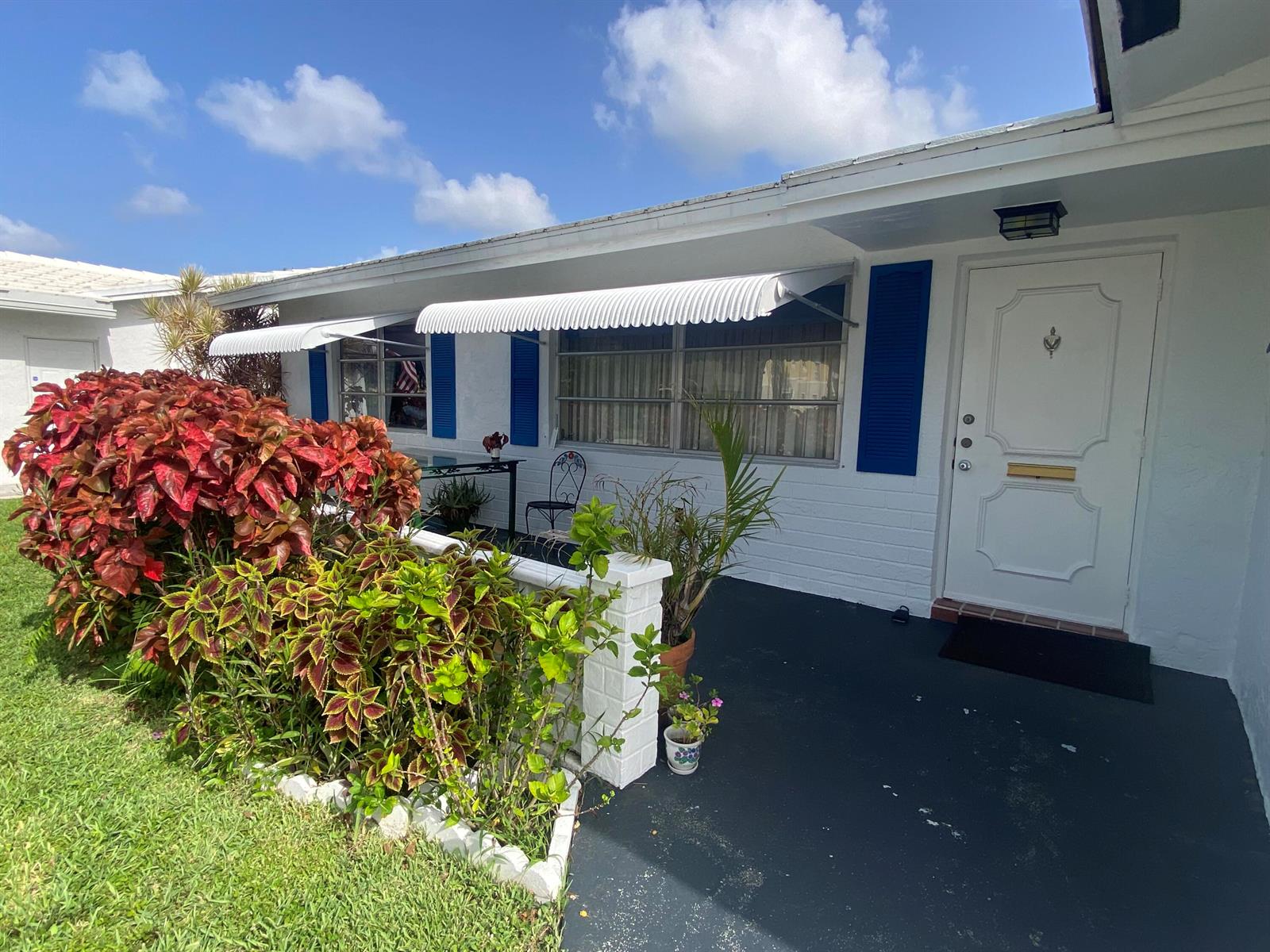 A white house exterior features blue shutters, metal awnings, and a landscaped front garden — 2300 SW 19TH Avenue, Boynton Beach FL 33426, BOYNTON BEACH, FL